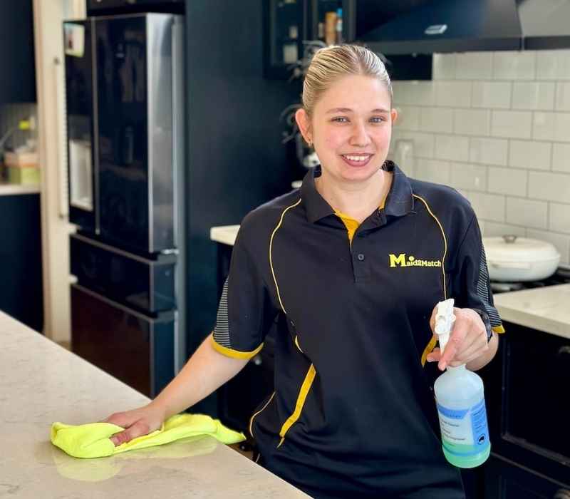 Maid2Match Brisbane professionally trained DVA cleaner Kate-lyn smiling while cleaning benchtop