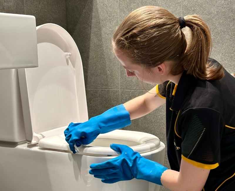 Maid2Match expert house cleaner wearing rubber gloves deep cleaning a toilet