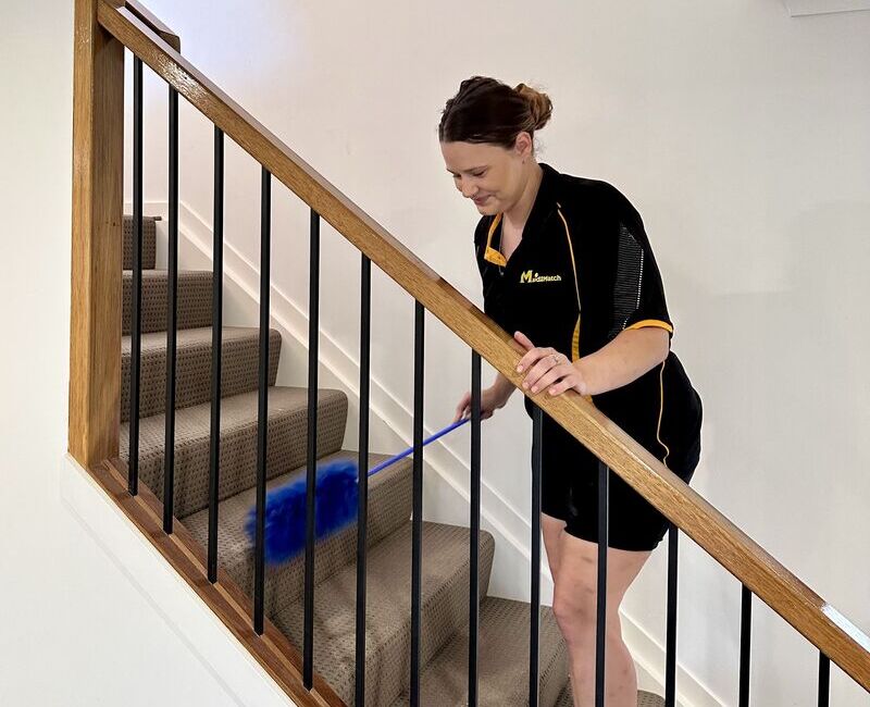 Professional cleaner Alison dusting the stairs railing