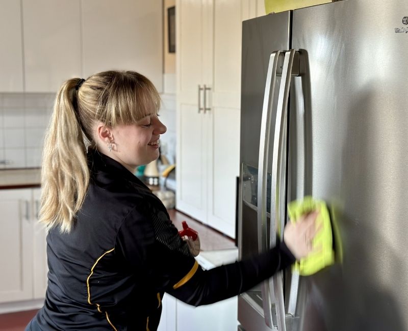 Maid2Match Geelong house cleaner Grace removing smudges from the stainless steel surface of a fridge with microfibre cloth
