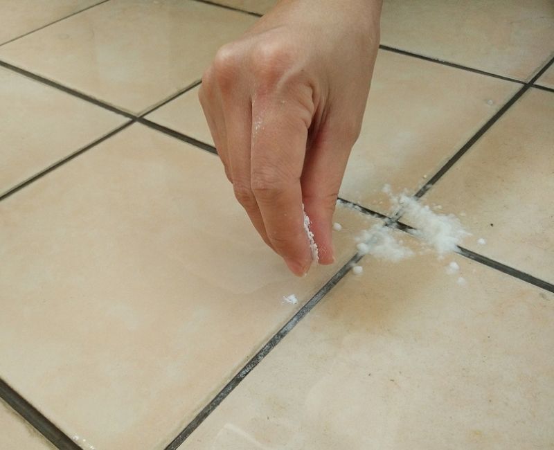 Hand poring bicarb soda on bathroom floor to spot test before cleaning