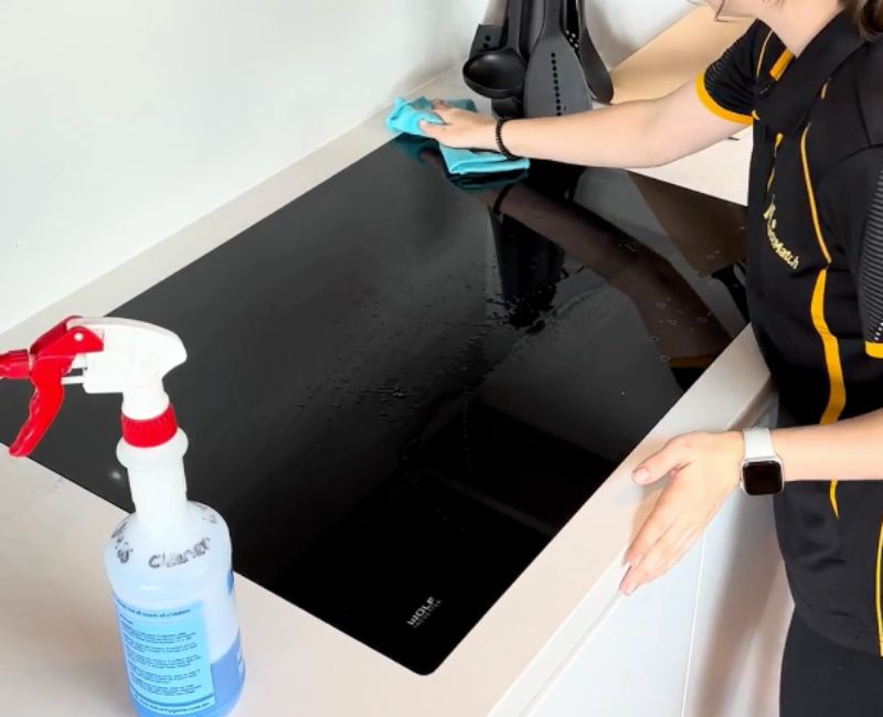 Maid2Match expert cleaner cleaning induction cooktop surface with cleaning spray and microfibre cloth