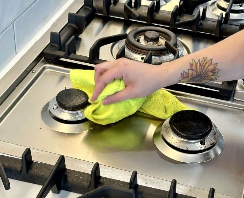 Maid2Match house cleaner cleaning baked on grease on a stainless steel cooktop