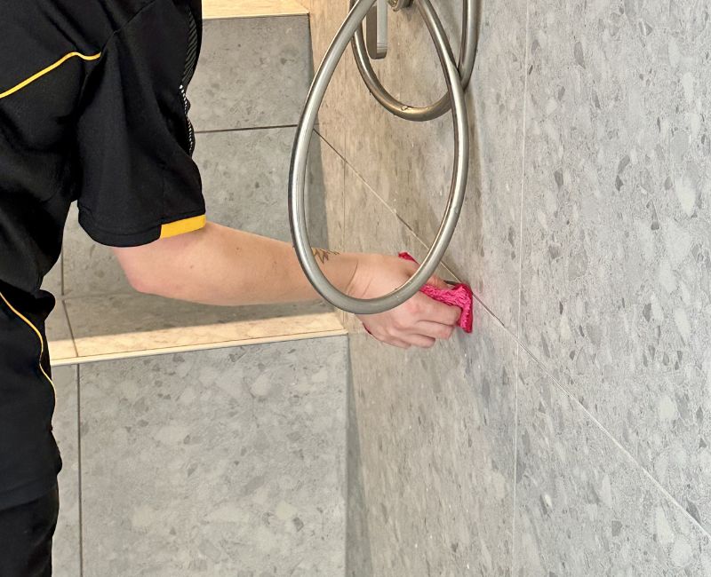 Maid2Match fully trained house cleaner drying tile grout lines in the shower with microfibre cloth