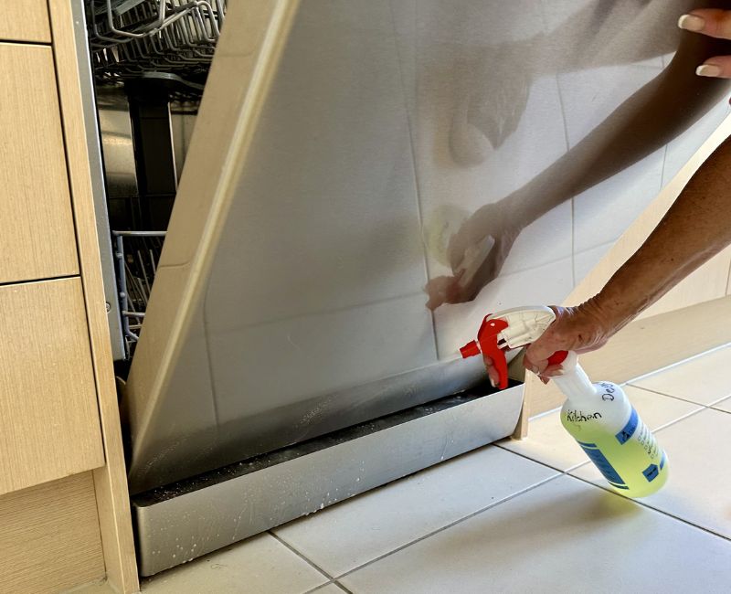 Maid2Match house cleaner spraying cleaning solution on dishwasher exterior