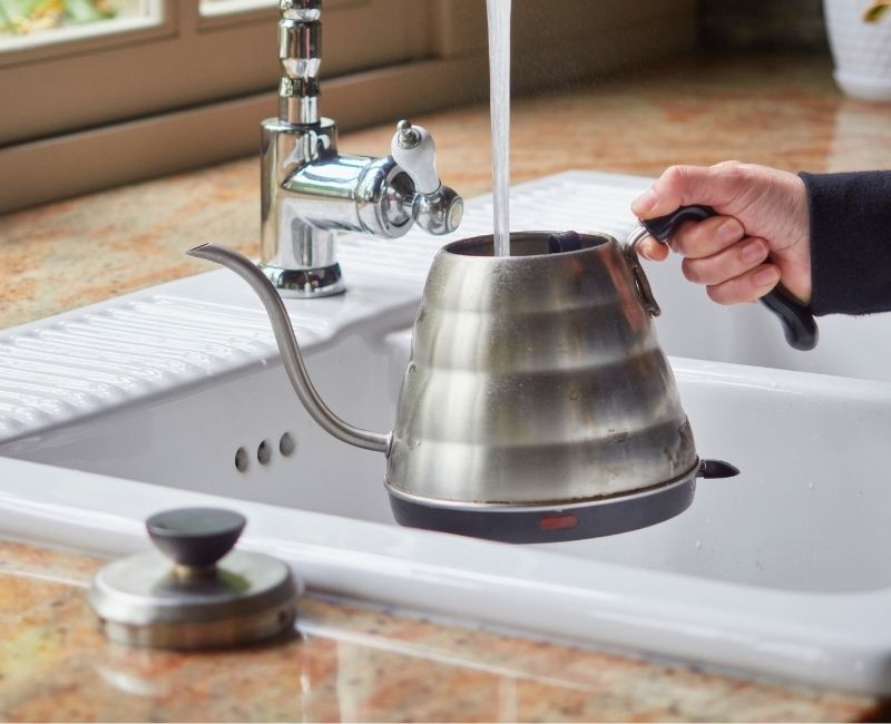 Rinsing a stainless steel gooseneck kettle under a kitchen tap