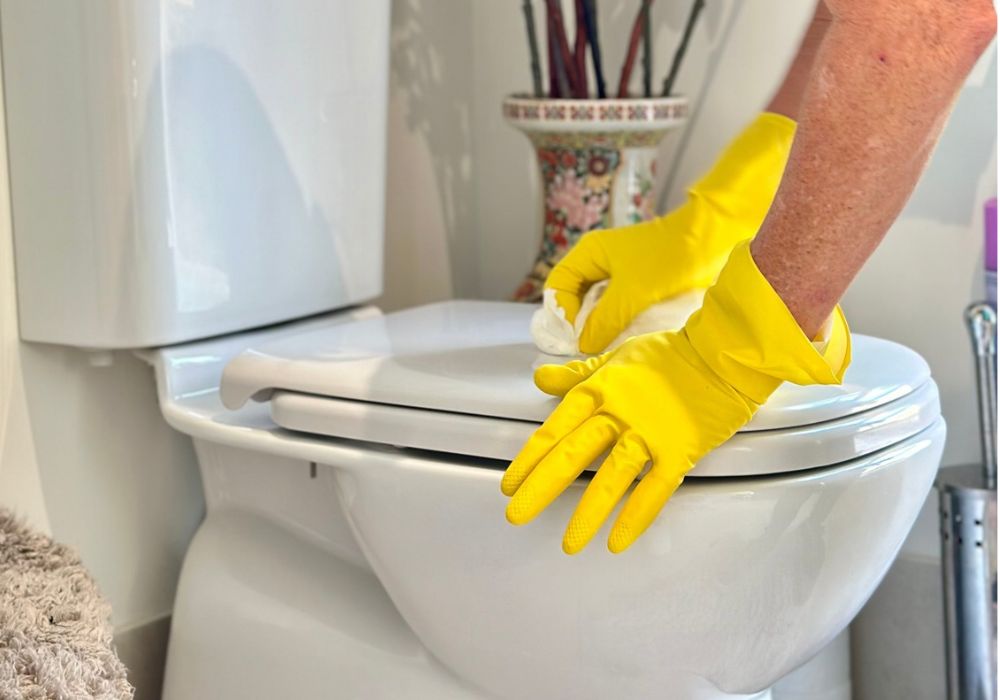 using-bleach-for-cleaning Hands wearing protective gloves cleaning a toilet lid