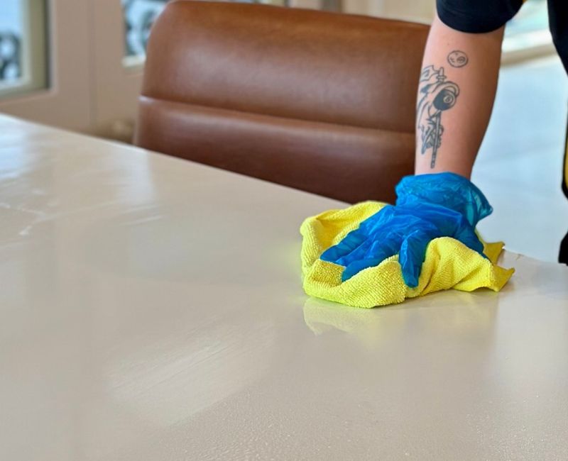 Hands wearing protective gloves wiping bleach off kitchen dining table